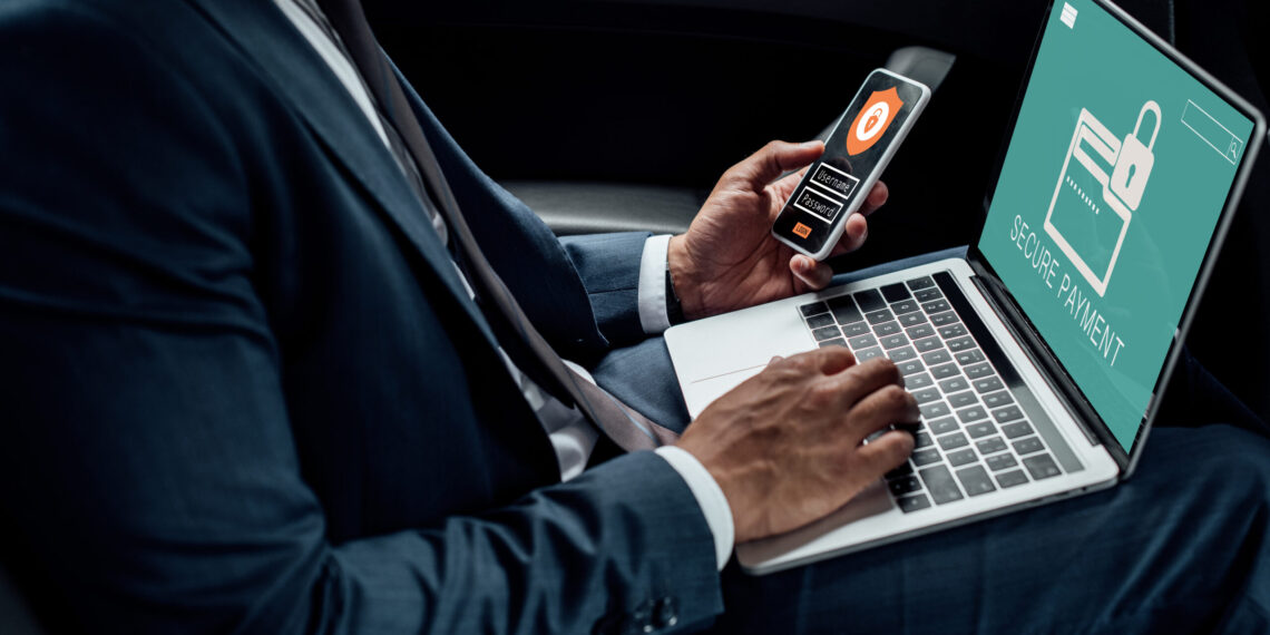 Cropped view of african american businessman using laptop and smartphone in car with cyber security